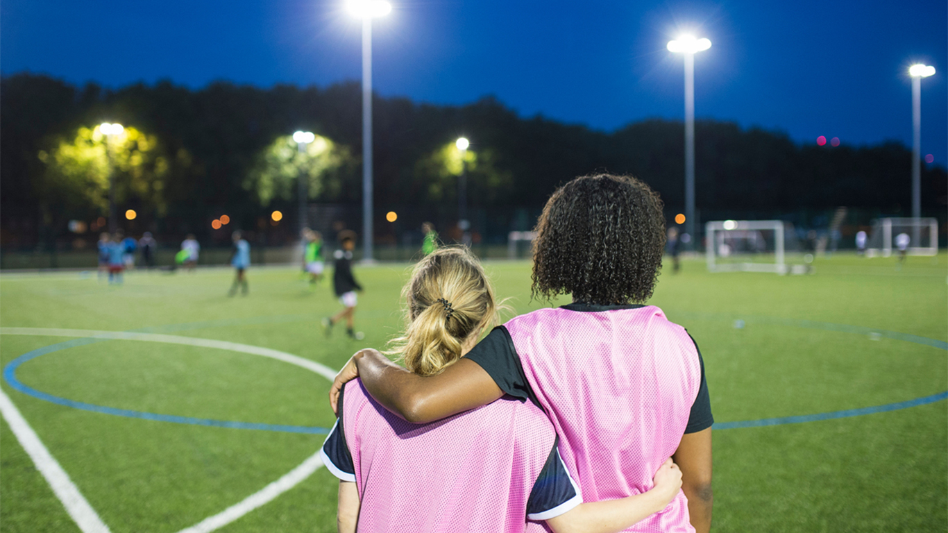 Two young soccer teammates look on at an ongoing game.